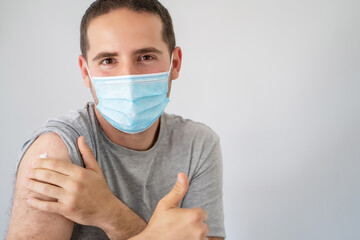 Young man with surgical mask and thumb up recently vaccinated with the Covid-19 vaccine