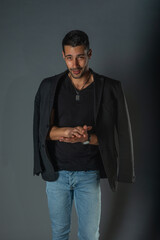 Handsome fashionable model in a black t-shirt with a jacket on his shoulders posing in a studio