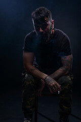 Fototapeta na wymiar Portrait of a handsome young tattooed man smoking a cigarette isolated in a studio on a dark background.