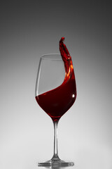 Glass with red wine and frozen splash on gray gradient background