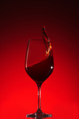 Glass with red wine and frozen splash on red gradient background