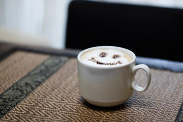 Coffee with milk and a smile in a cup on a napkin on a wooden table.