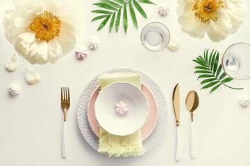 Summer birthday dinner table setup. Pale yellow peony flowers and Late Spring, Summer flat lay. White dinner table, white and gold utensils, decorated with peony flowers and palm leaves.