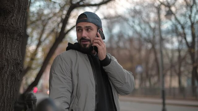 Young, modern handsome man talking on the phone on the street of a small town on a sunny spring day.