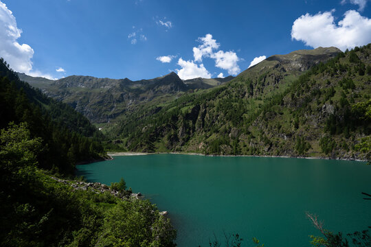Splendid view of the Lago dei Cavalli, Alpe Cheggio. The teal water, the rich vegetation, the blue sky and the white clouds.