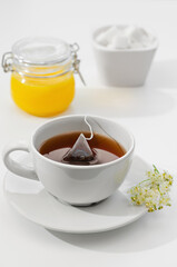 Cup of hot tea is brewed from a tea bag. Flowers on a saucer, honey and sugar in the background. Shallow depth of field