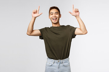 Portrait of optimistic, happy asian man in green t-shirt inviting people check-out advertisement,...