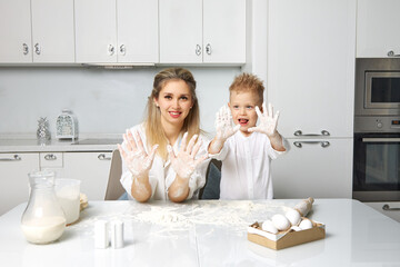 Obraz na płótnie Canvas Happy mom and baby cook in a white kitchen at a table made of dough, they are very good and fun together