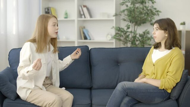 Emotional female friends having fight on a couch, gesturing with hands, argument