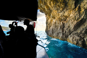 Unidentifiable tourists seen in silhouette in a boat inside the Blue Eye Cave near Paleokastritsa...