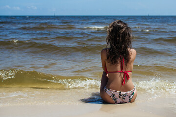 Beautiful young woman sits on the beach in sea water on a sunny summer day. Summer background.