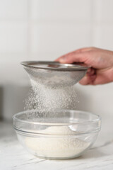 Close-up of a woman's hands sifting flour through a sieve.