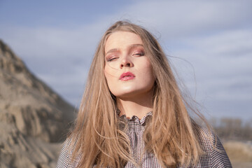 Beauty portrait of a young blond girl in a vintage dress. She is posing on a sandy landscape.