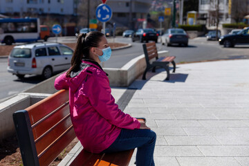 A woman at the time of a virus pandemic is sitting alone on a park bench in a park