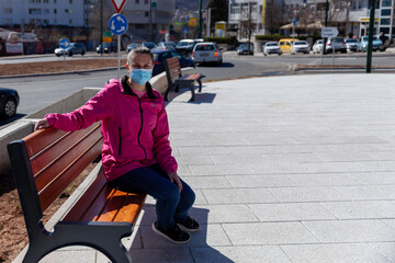 A woman at the time of a virus pandemic is sitting alone on a park bench in a park