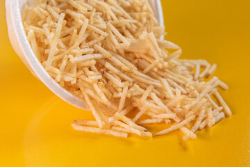 White bowl with potato straw on yellow background
