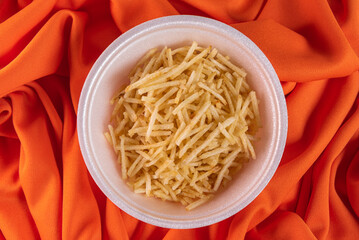 White bowl with potato straw on orange background