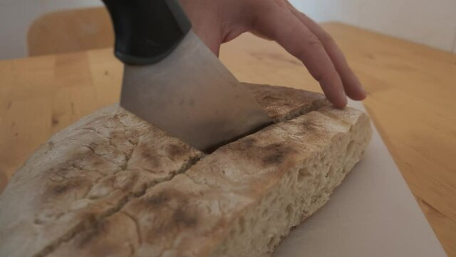 Hands cut traditional bread from Madeira called bolo do caco on wooden table. Close up 