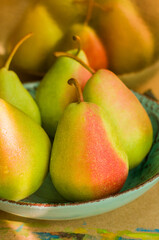 Green pears with red sides lying on a turquoise plate in the sunlight. 