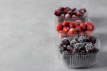 Frozen berries such as cherries, strawberries and blackberries in the storage boxes on the light gray background. Copy space