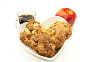 Wholemeal baked cookies in a bowl in the shape of a heart and apple with black coffee