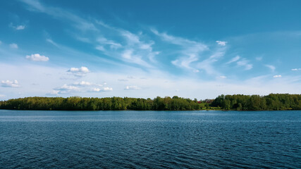 Summer landscape with green trees on river bank and ripples on the water. Beautiful blue sky with cirrus and cumulus clouds.