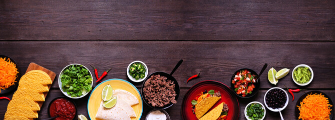 Taco bar bottom border with assorted ingredients. Top view on a dark wood banner background....