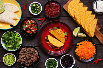 Taco bar table scene with a selection of ingredients. Above view on a dark wood banner background....