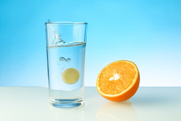 effervescent vitamin C tablet dissolves in water. a glass of water, effervescent tablet and orange on blue background. vitamin C concept