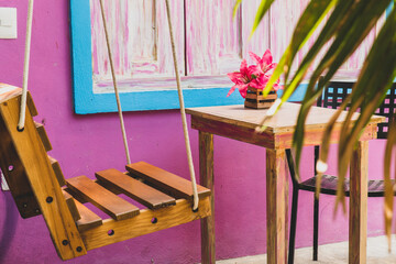 Colourful painted pink wall with a wooden swing rocking chair on a outdoor patio terrace in Tulum in Mexico - obrazy, fototapety, plakaty