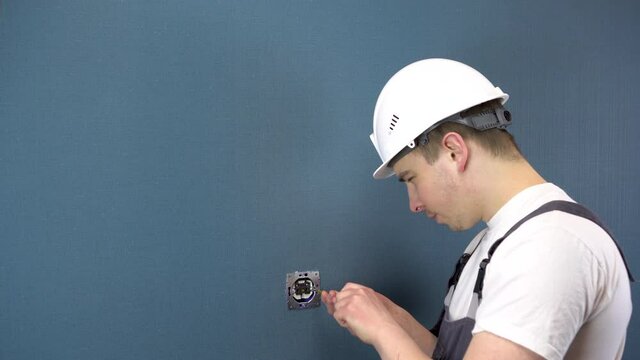 An electrician repairs an outlet in the house. A man in special clothing and a helmet installs an outlet.