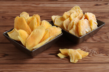Dried pieces of mango and jackfruit lying on a brown ceramic bowls on a wooden table. Macro. Closeup
