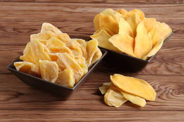 Dried pieces of mango and jackfruit lying on a brown ceramic bowls on a wooden table. Macro. Closeup