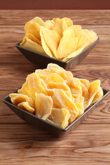 Dried pieces of mango and jackfruit lying on a brown ceramic bowls on a wooden table. Macro. Closeup