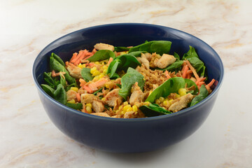 Healthy spinach salad in bowl with chopped baked chicken breast pieces, corn kernels, carrots and crispy onions