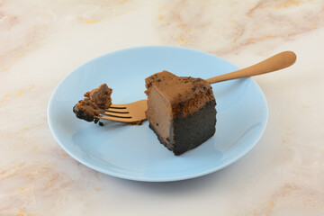 Slice of Belgian chocolate cheesecake with missing bite and copper fork on blue dessert plate