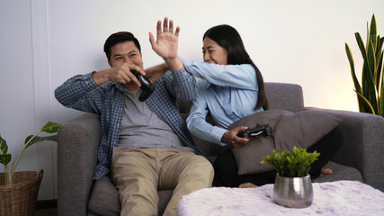 Excited funny young couple playing video games holding game controller sitting on sofa having fun...