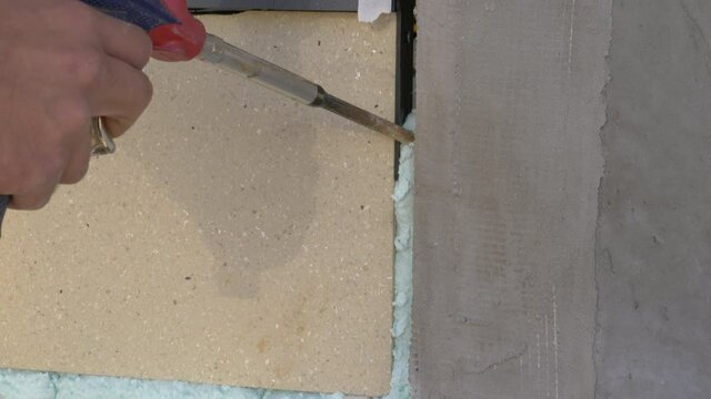 CLOSE UP: Builder mounting windows sprays polyurethane foam into a small gap between the wall and a window. Detailed shot of a foam gun spraying blue sealant into a crease in the unfinished wall.