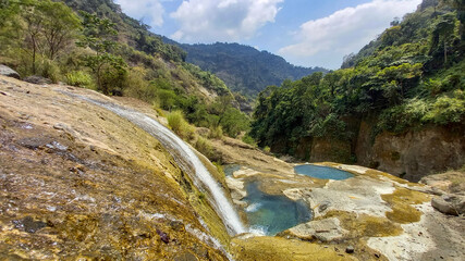 Wide shot of waterfall and aqua-blue pools in the middle of forested mountains in the rainforest of northern Luzon, Philippines