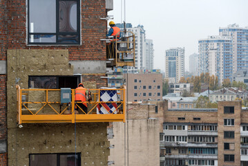 High rise construction work. Construction site workers in cradles working with facade. Suspended...
