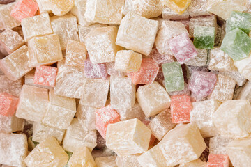 A many of colored cubes in powdered sugar. Turkish delight or lokum is a confections based on a gel of starch and sugar. The concept of oriental sweets. Selective focus.