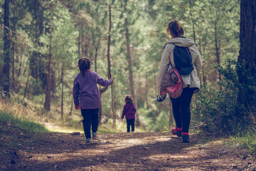 Mother and her two young daughters hiking in the woods on a cold autumn day in a red coat. Active family holidays with children.