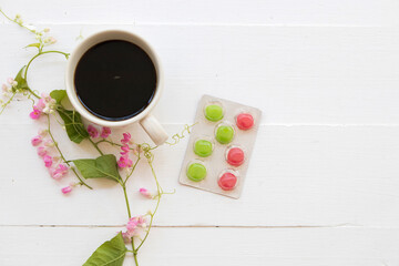 hot coffee with lozenge for health care sore throat, pink flowers arrangement flat lay style on background white wooden