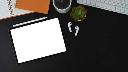 Top view of office desk with mock up digital tablet, coffee cup, keyboard and notebook on black leather.