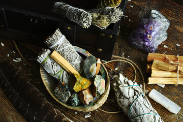 A close up image of white sage smudge sticks with rough crystals and selenite on a dark wooden...