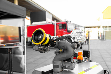 Modern high-tech firefighting robot with a hose for penetration into especially dangerous areas and extinguishing fires near red fire truck. Technology, transport and robotics concept