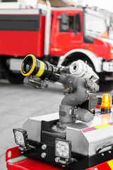 Modern high-tech firefighting robot with a hose for penetration into especially dangerous areas and extinguishing fires near red fire truck. Technology, transport and robotics concept