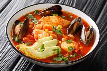 Sopa de Mariscos seafood soup with cod, shrimp, mussels, vegetables and avocado close-up in a bowl on the table. Horizontal