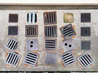 Several iron exhaust grills are placed in a row on the sidewalk near the restaurants.