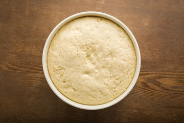 Fresh white raw dough in bowl on dark brown wooden table background. Ready for baking. Closeup. Top down view.